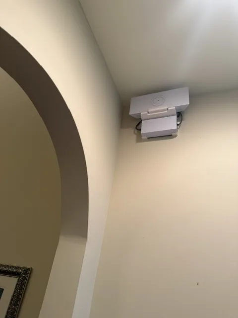 White Starlink unit mounted high on a wall beside a plaster archway, angled down into the room.