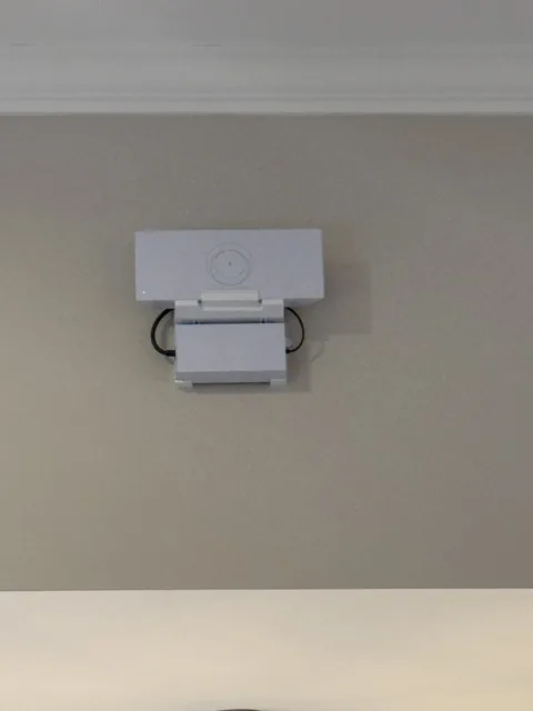 White Starlink unit wall mounted on its bracket, set tight against the ceiling trim of a painted interior wall.