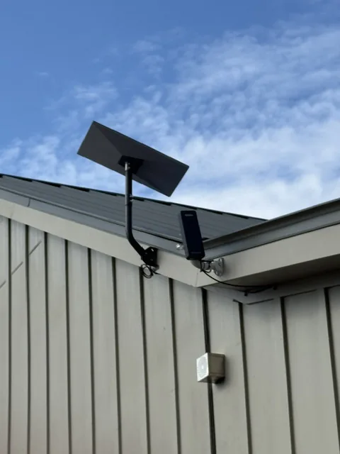 Starlink mounted on the eave of a metal roofed shop against a blue sky.